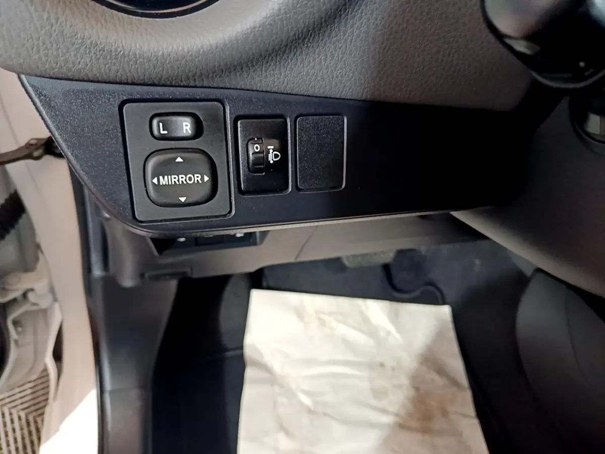 Vue rapprochée des commandes de réglage des rétroviseurs et des phares dans une Toyota Yaris blanche 2019.