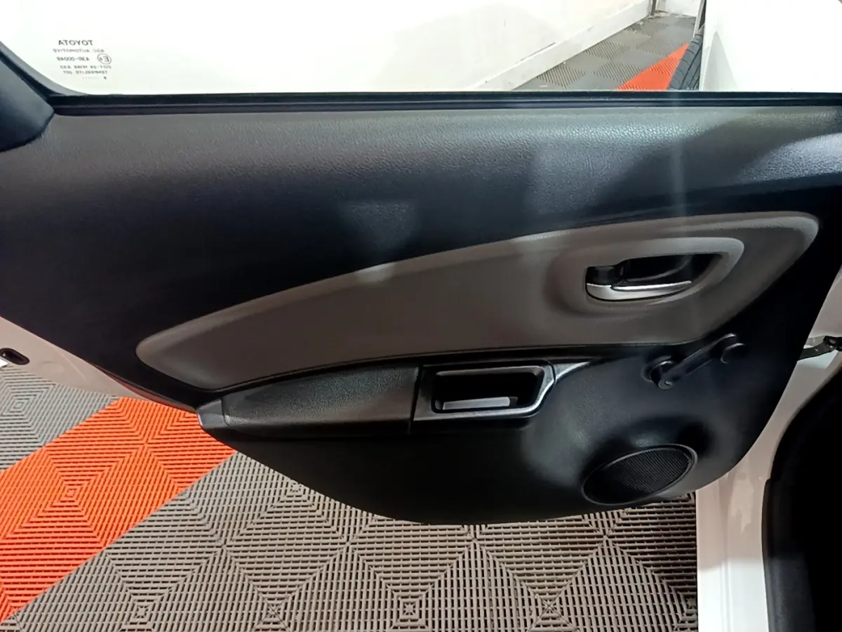 Gros plan sur la porte intérieure côté gauche de la Toyota Yaris blanche, montrant la poignée et le haut-parleur.