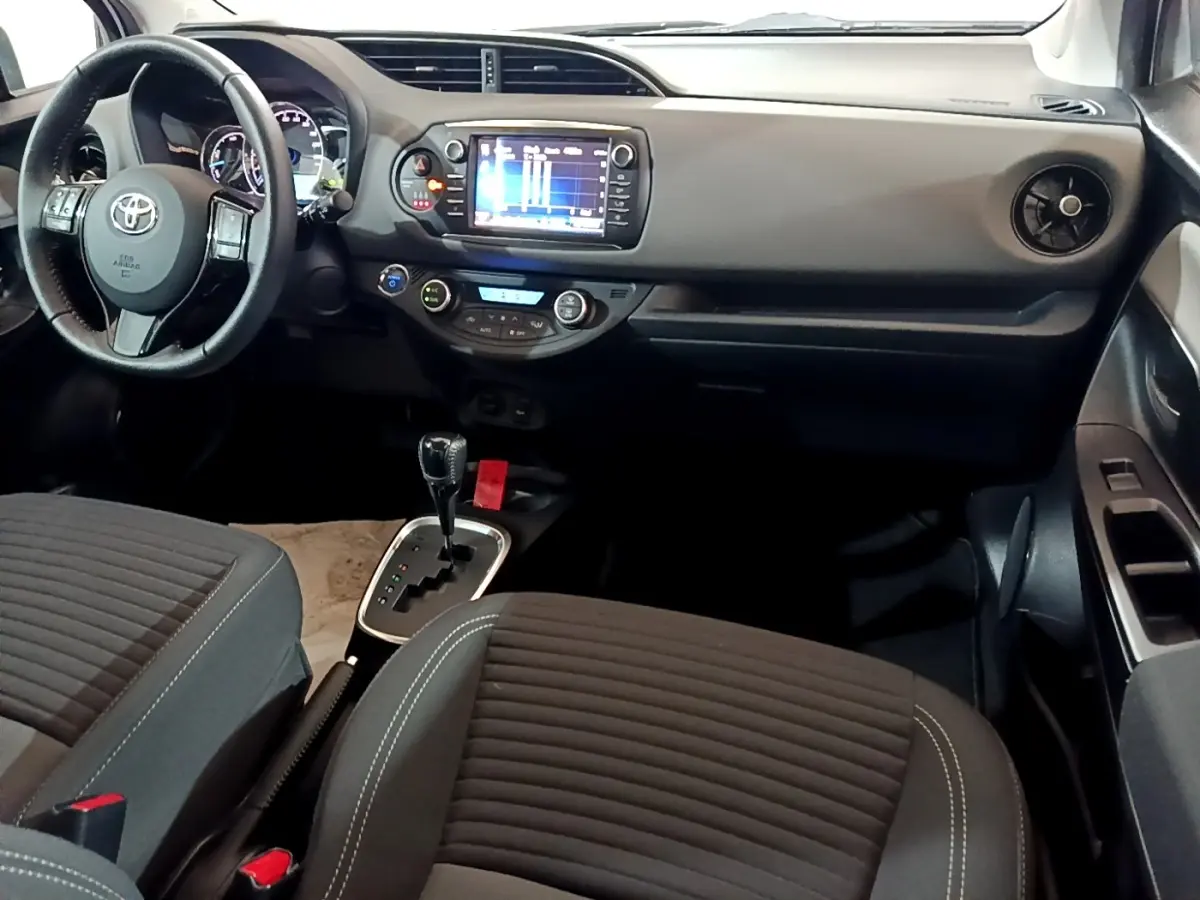 Vue intérieure avant droite de la Toyota Yaris 2019, tableau de bord noir avec écran tactile et sièges tissu gris foncé.