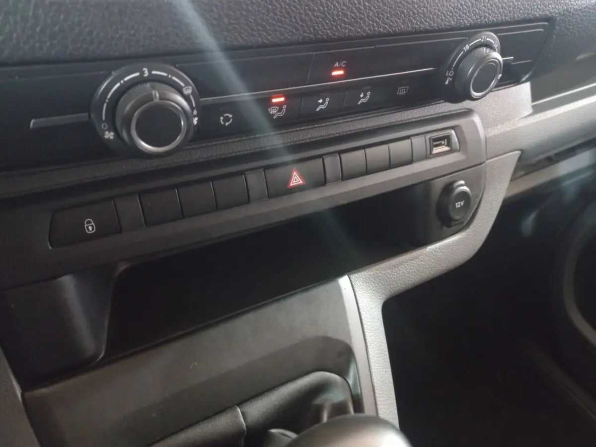 Gros plan sur la console centrale du Peugeot Traveller gris clair, avec commandes climatisation et port USB visible.