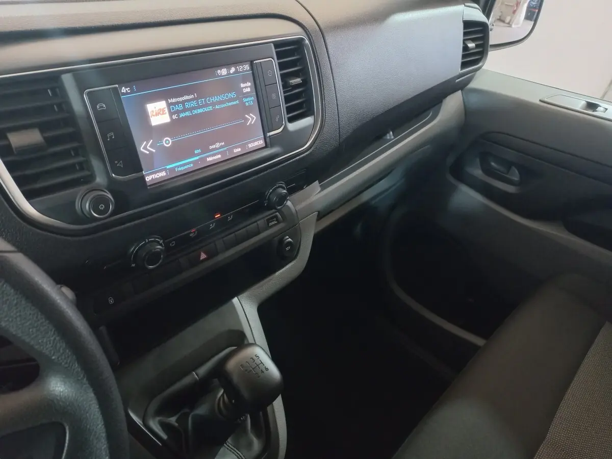 Vue intérieure côté passager du tableau de bord gris clair du Peugeot Traveller avec écran tactile et levier de vitesses manuel.