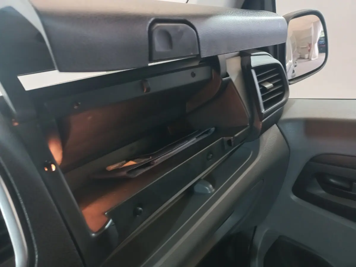 Gros plan sur la boîte à gants ouverte côté passager du Peugeot Traveller 2021, intérieur gris foncé.