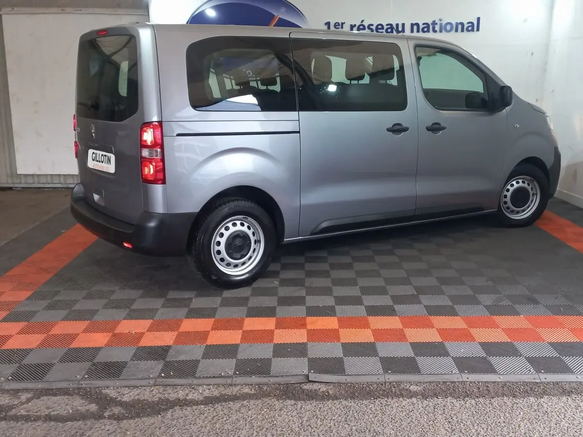 Vue latérale droite d’un Peugeot Traveller gris clair 2021 avec vitres arrière teintées et jantes acier simples.