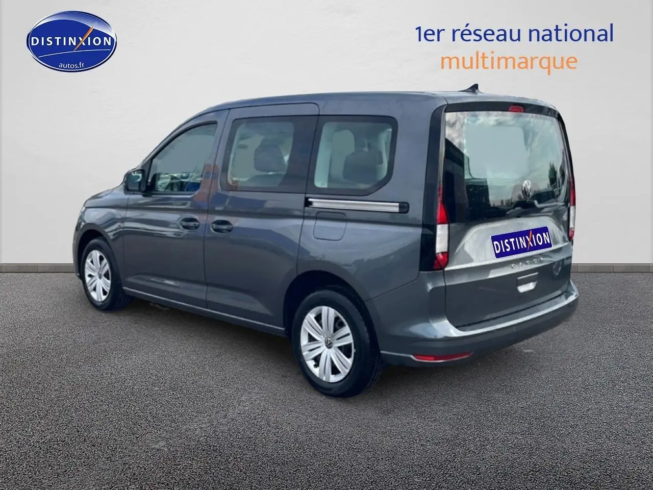 Vue 3/4 arrière droite d'un Volkswagen Caddy gris indien 2025 avec vitres teintées et barres de toit.