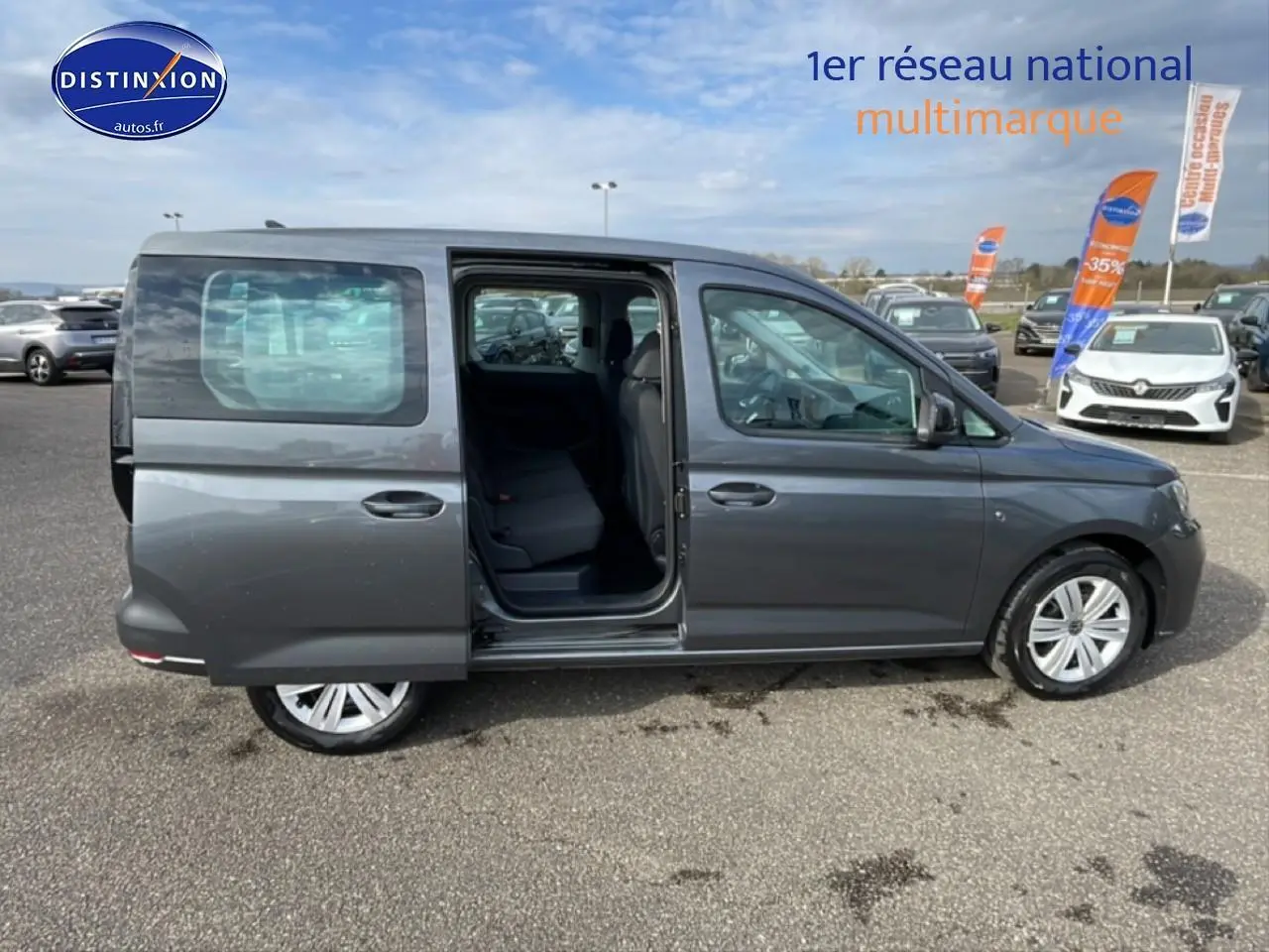 Profil droit d’un Volkswagen Caddy gris indien 2025 avec porte coulissante arrière ouverte sur parking.