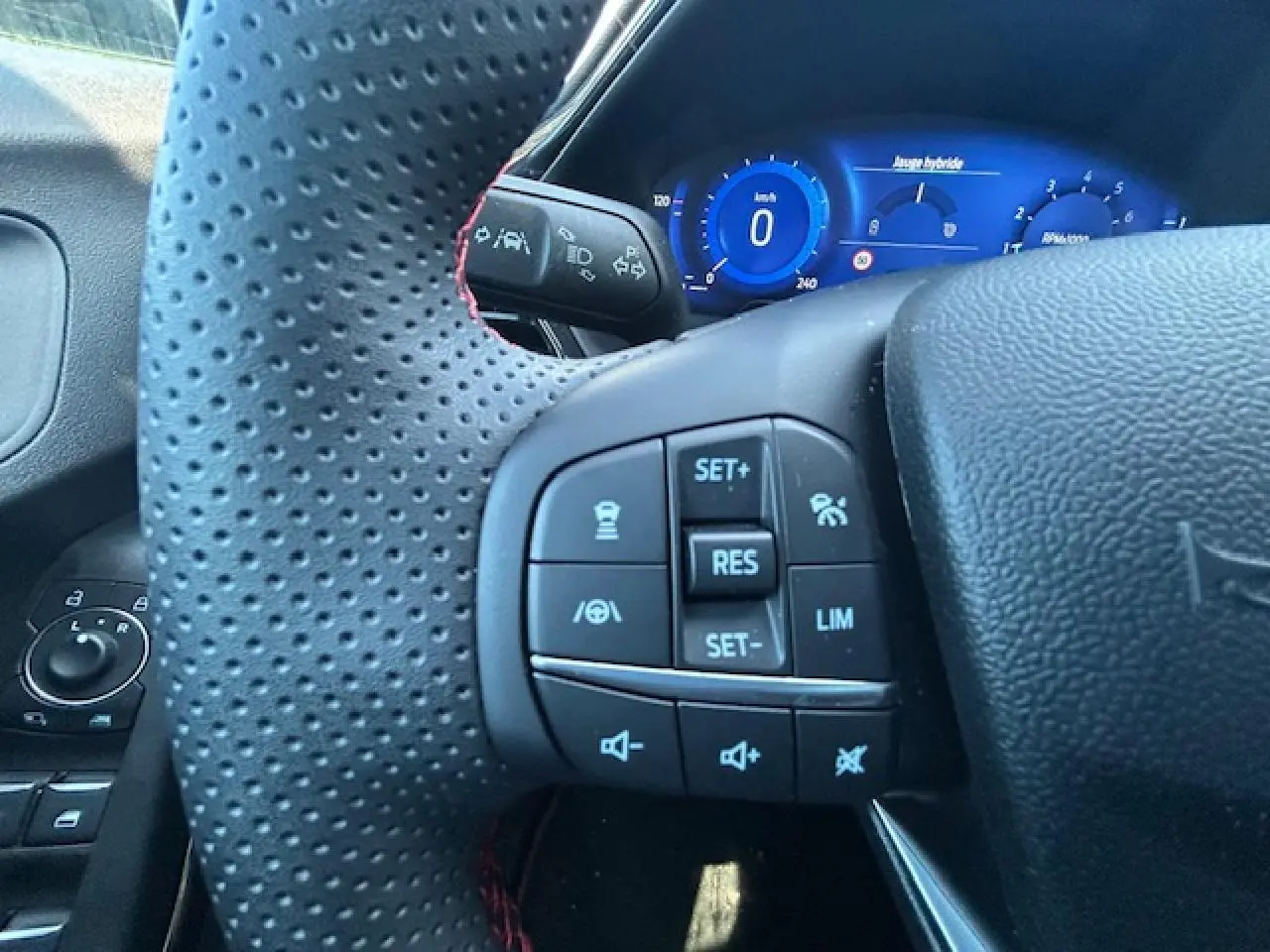 Gros plan sur le volant perforé noir avec surpiqûres rouges et commandes multifonctions, tableau de bord numérique bleu en arrière-plan.