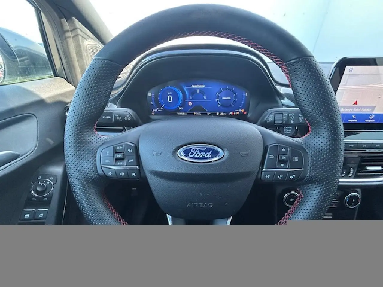 Vue intérieure centrée sur le volant perforé noir avec surpiqûres rouges du Ford Puma gris, tableau de bord numérique et écran tactile.