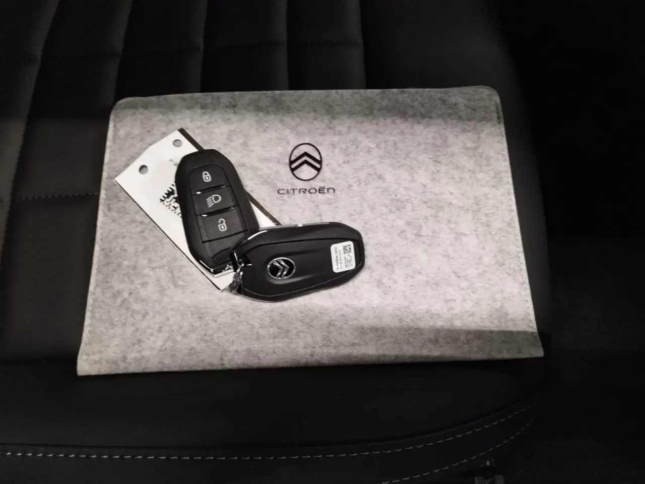 Clé de voiture Citroën posée sur un étui gris avec logo, sur siège noir en cuir, vue rapprochée intérieure.