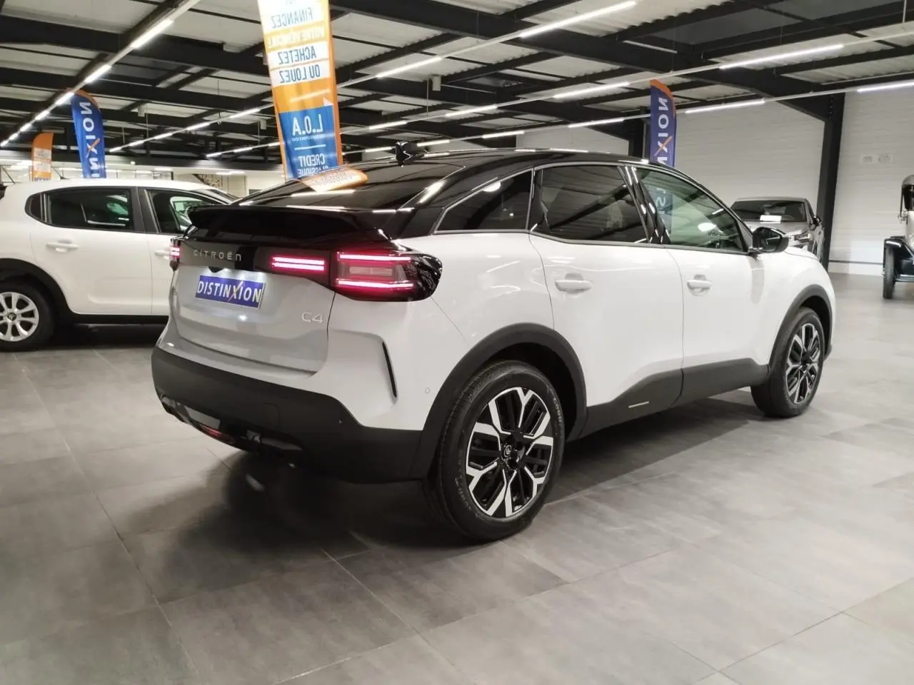 Vue 3/4 arrière droite d'une Citroën C4 blanche Okenite avec toit noir et jantes alliage 18'' dans un showroom.