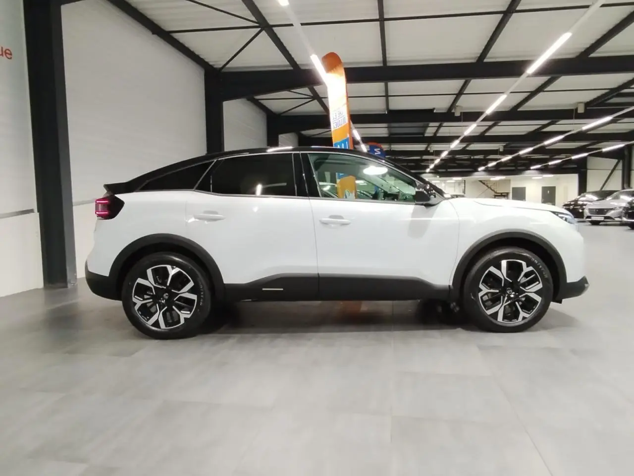 Vue latérale droite d'une Citroën C4 blanche Okenite avec toit noir et jantes alliage 18 pouces en intérieur showroom.