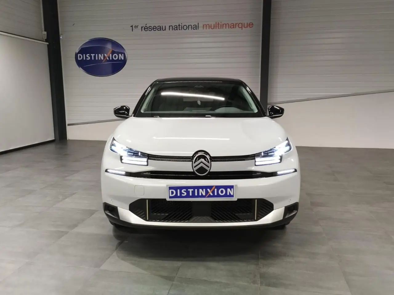 Vue avant d'une Citroën C4 blanche Okenite avec toit noir, feux LED allumés, en intérieur showroom.