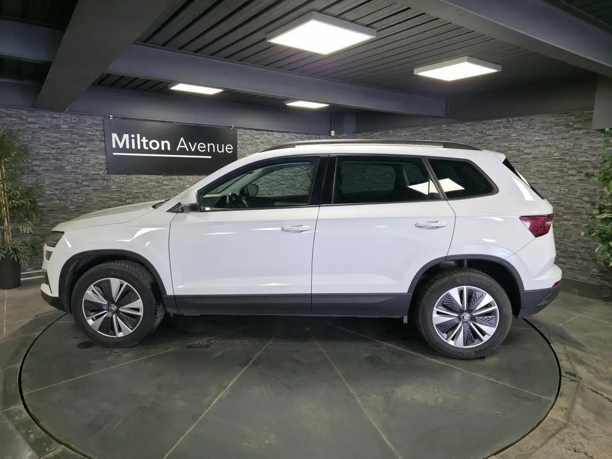 Vue latérale droite d'un Skoda Karoq blanc 2023 avec jantes alliage 17'' et barres de toit noires.