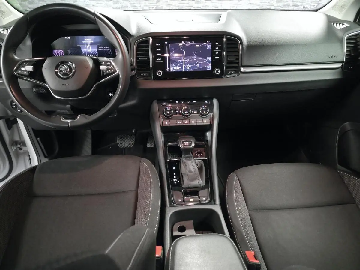 Vue intérieure avant du Skoda Karoq 2023, tableau de bord noir avec écran tactile et volant cuir multifonctions.