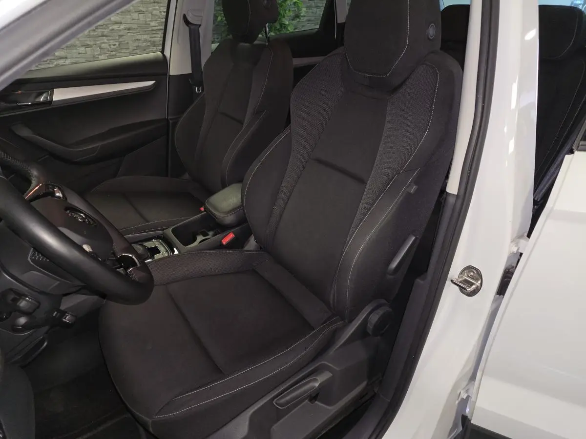 Vue intérieure côté gauche du Skoda Karoq blanc 2023, sièges avant noirs avec coutures contrastées et volant cuir.