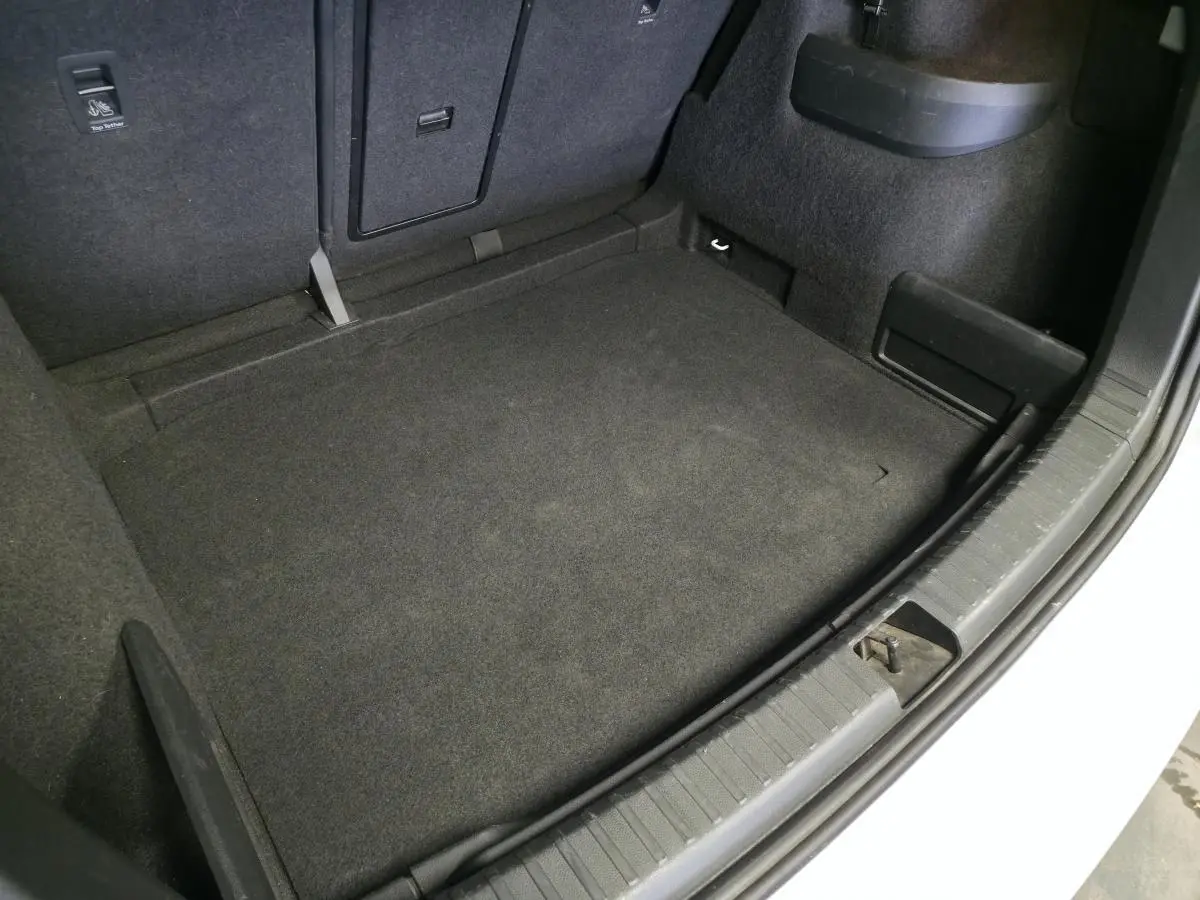Coffre ouvert vu de dessus d’un Skoda Karoq blanc 2023, avec tapis de sol noir et compartiments latéraux.