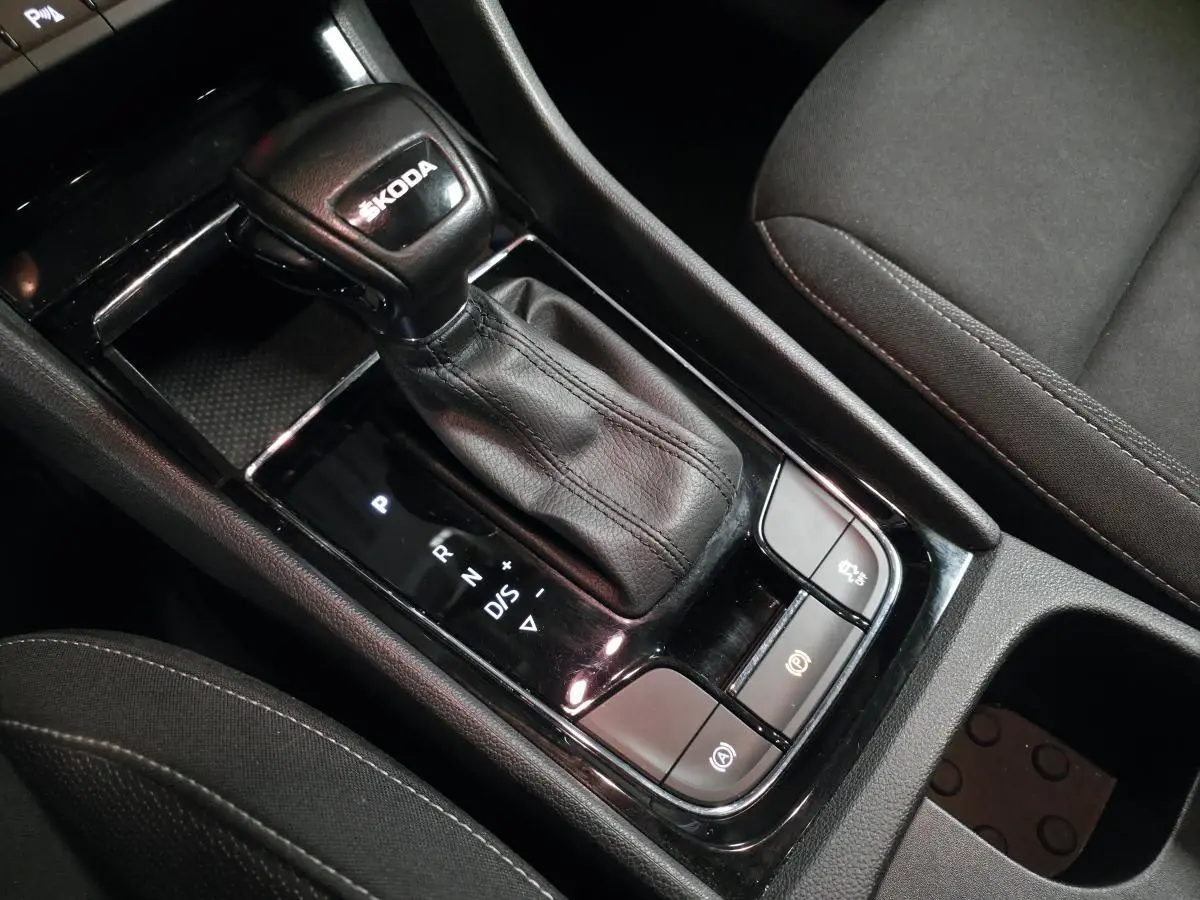 Gros plan sur le levier de vitesses automatique noir en cuir avec logo ŠKODA, entouré de commandes dans l'habitacle sombre.