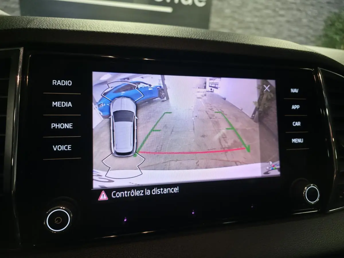 Écran de caméra de recul montrant une Skoda Karoq blanche vue de dessus en stationnement arrière.