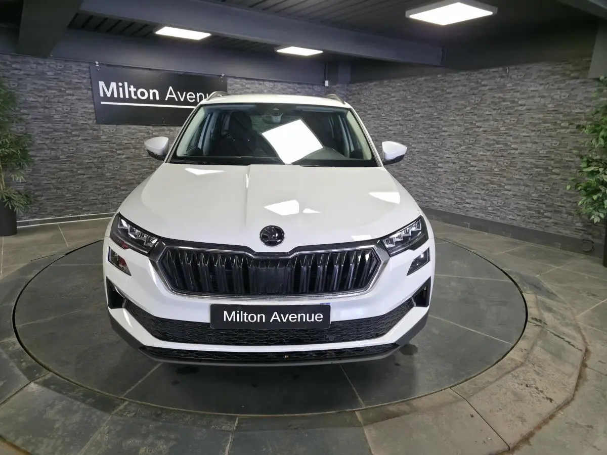 Vue avant d'un Skoda Karoq blanc 2023 avec calandre noire et phares LED dans un showroom.