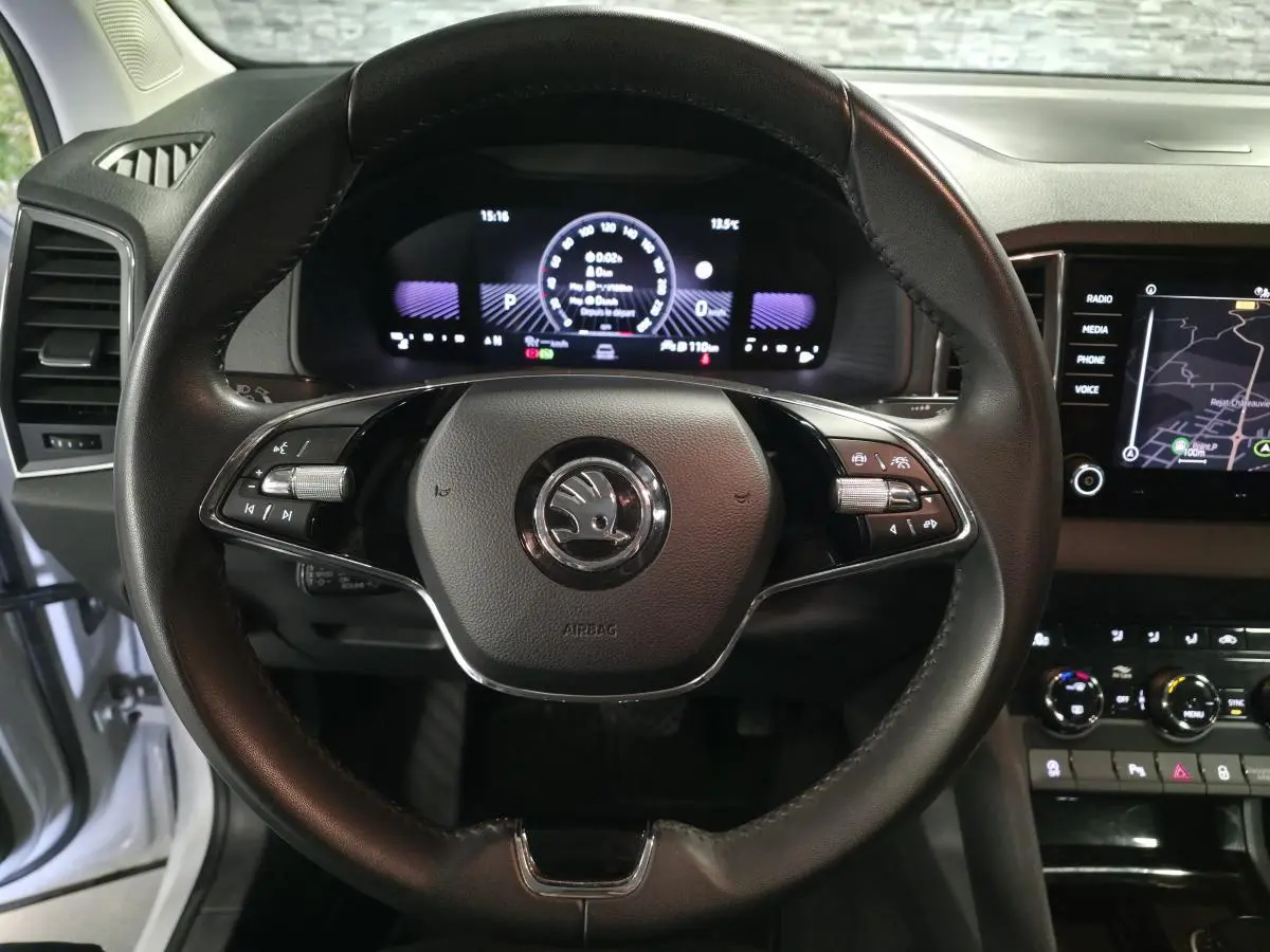 Vue rapprochée du volant cuir noir et du tableau de bord numérique du Skoda Karoq blanc 2023, affichage navigation visible.