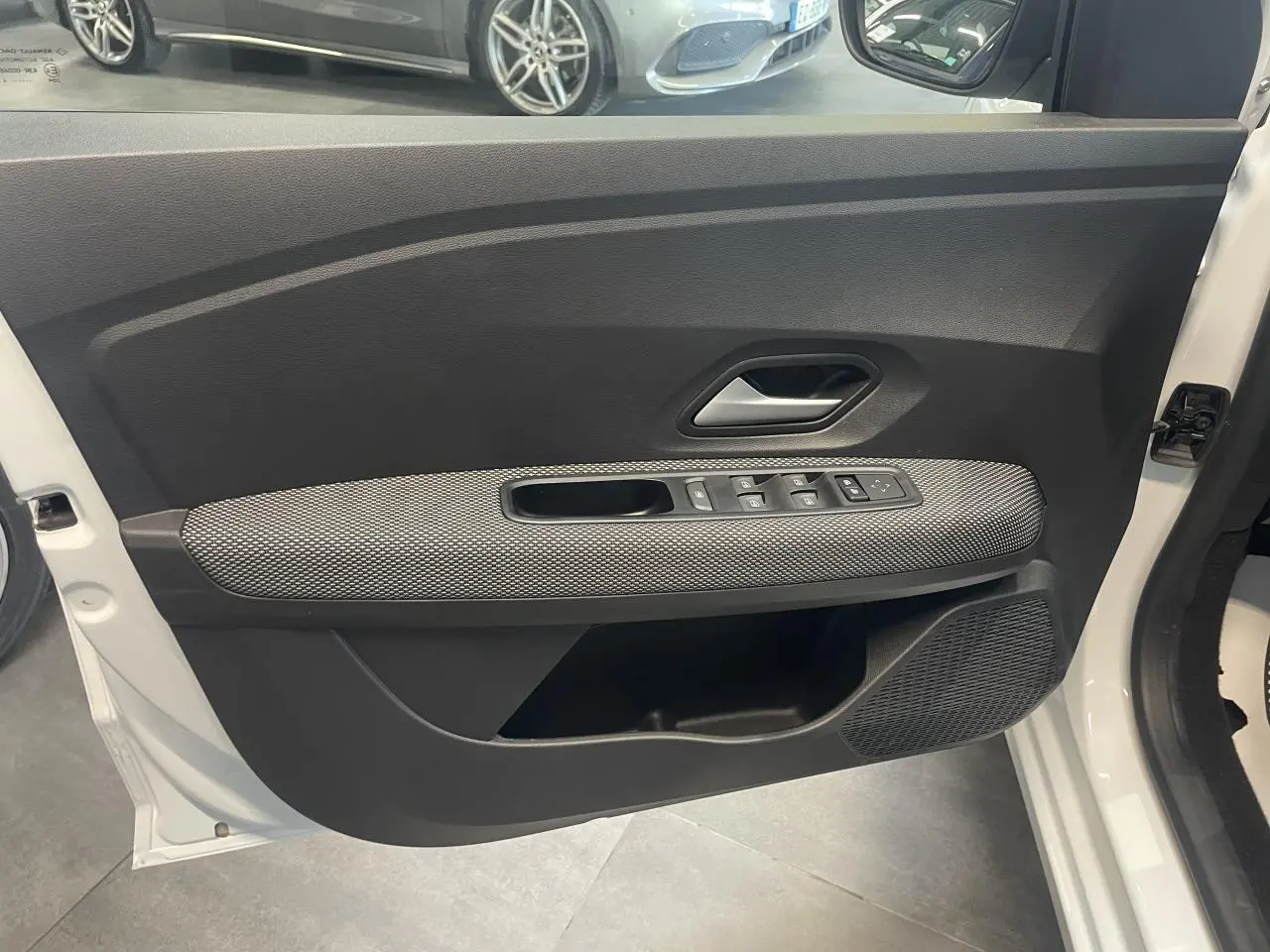 Vue rapprochée de la porte avant gauche blanche d’une Dacia Sandero 2024 avec commandes de vitres et poignée grise.