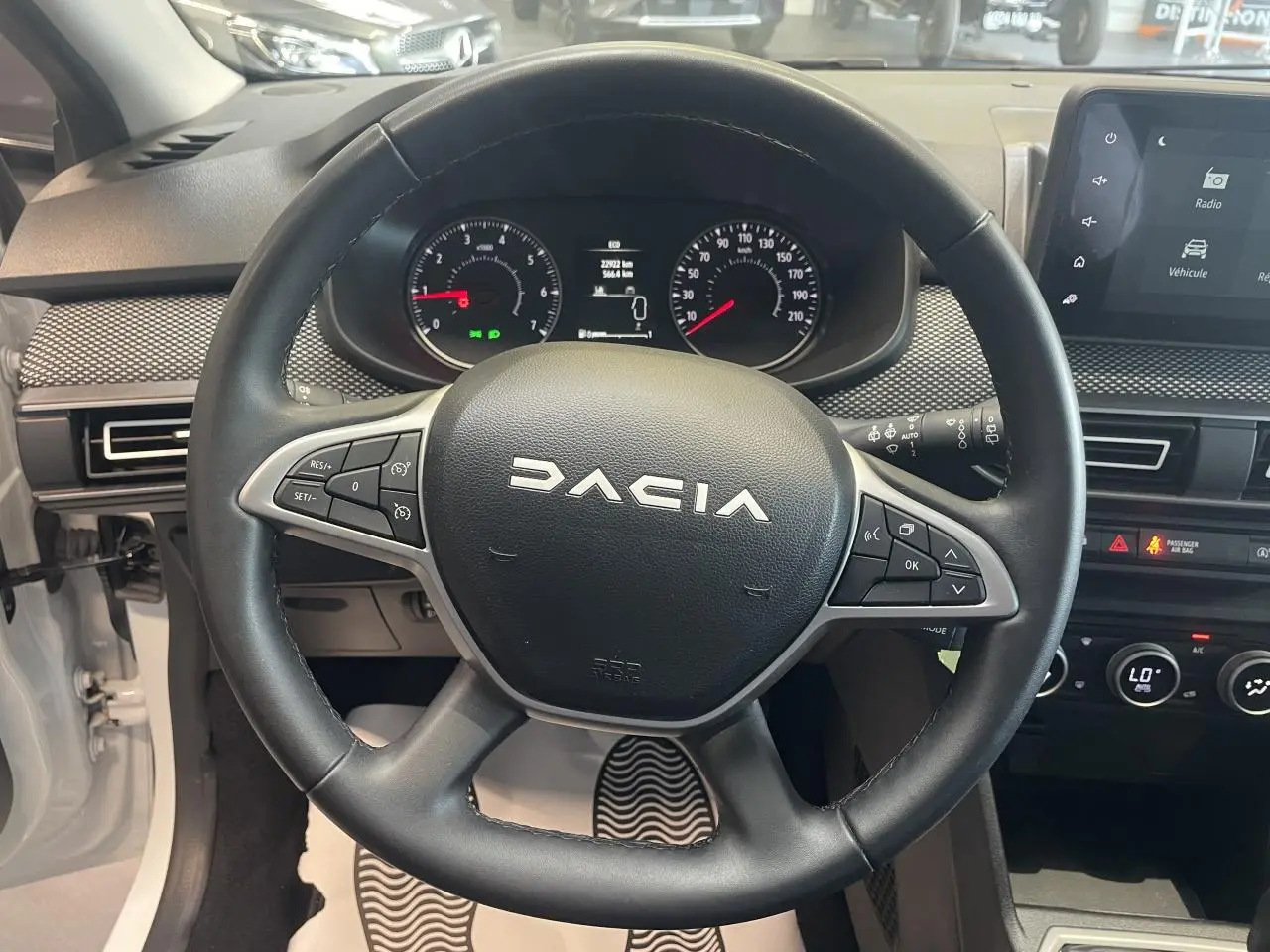 Vue intérieure centrée sur le volant noir DACIA avec tableau de bord et écran tactile du Sandero blanc 2024.