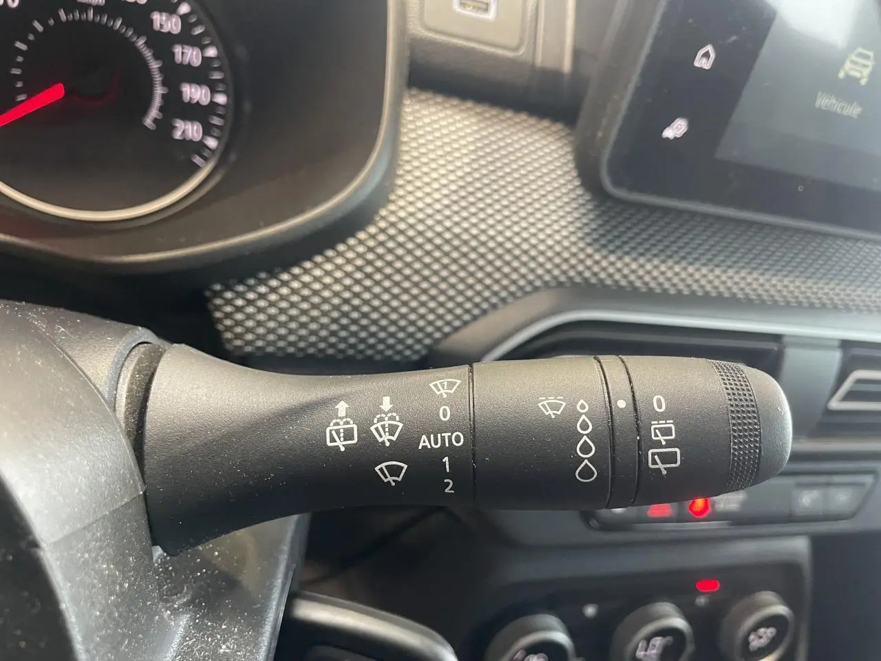 Gros plan sur la commande des essuie-glaces du tableau de bord d’une Dacia Sandero blanche 2024.