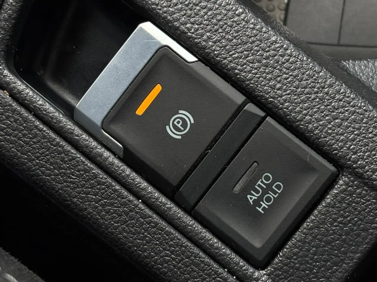 Gros plan sur le bouton de frein de stationnement électromécanique et fonction Auto Hold dans l’habitacle noir du Volkswagen T-Roc.