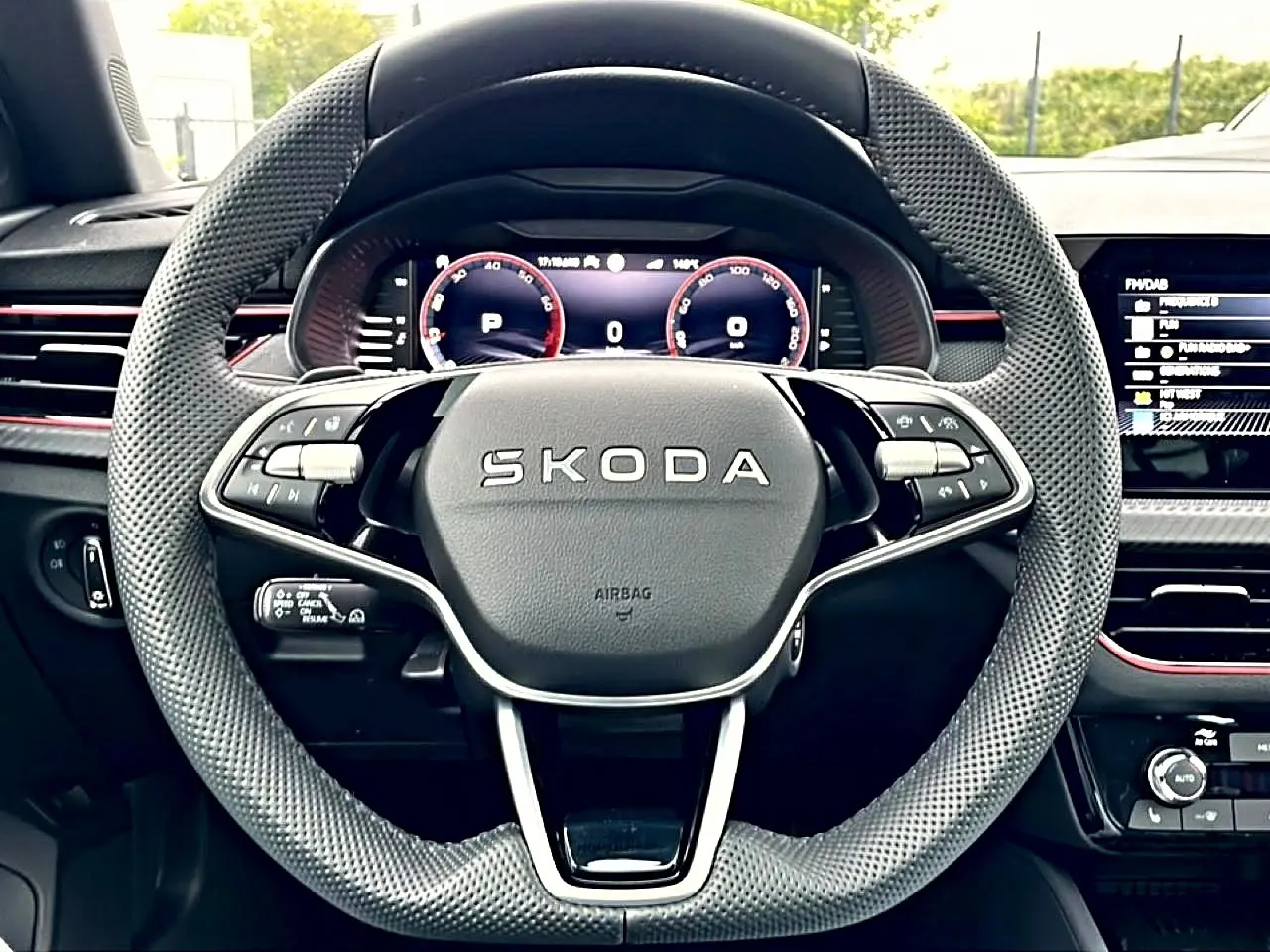 Vue rapprochée du volant cuir perforé SKODA avec tableau de bord numérique et inserts rouges sur fond noir.