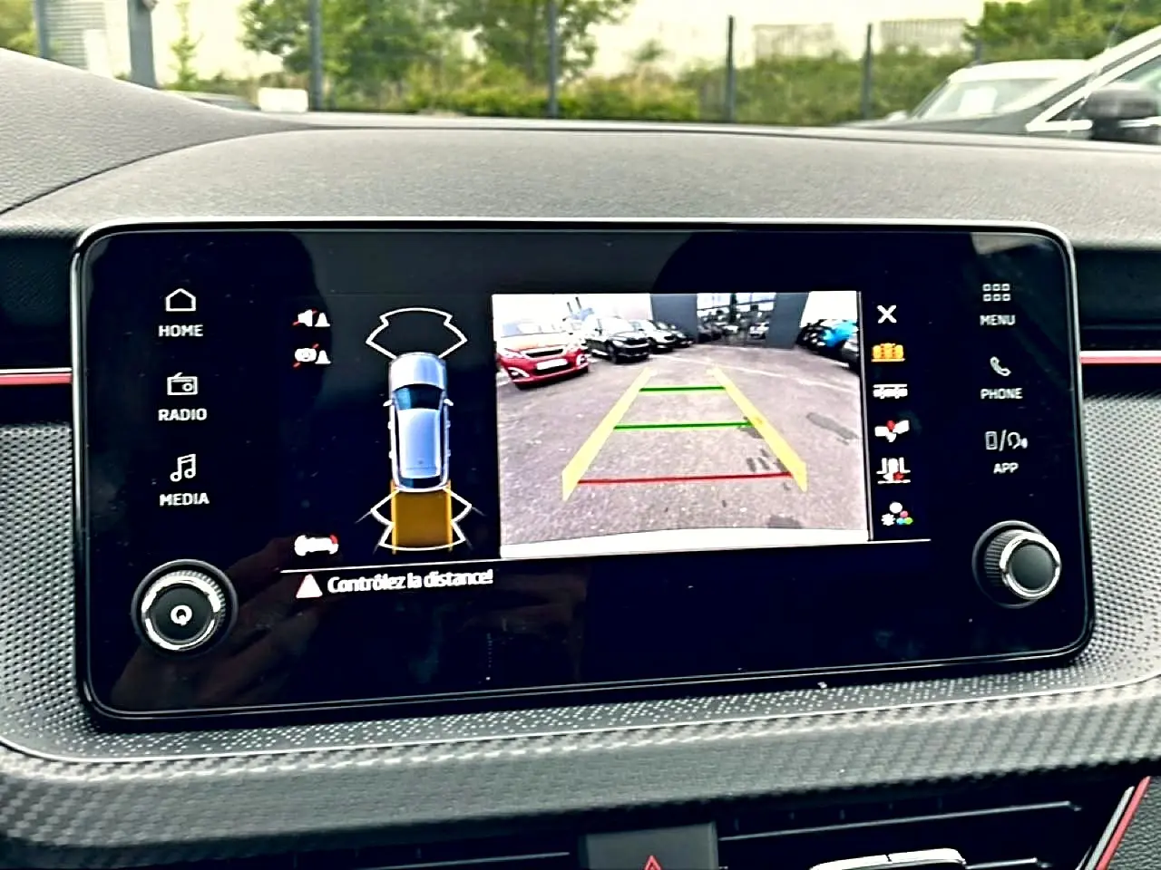 Écran tactile intérieur montrant la caméra de recul et l’aide au stationnement du Skoda Kamiq blanc nacré, vue de face.