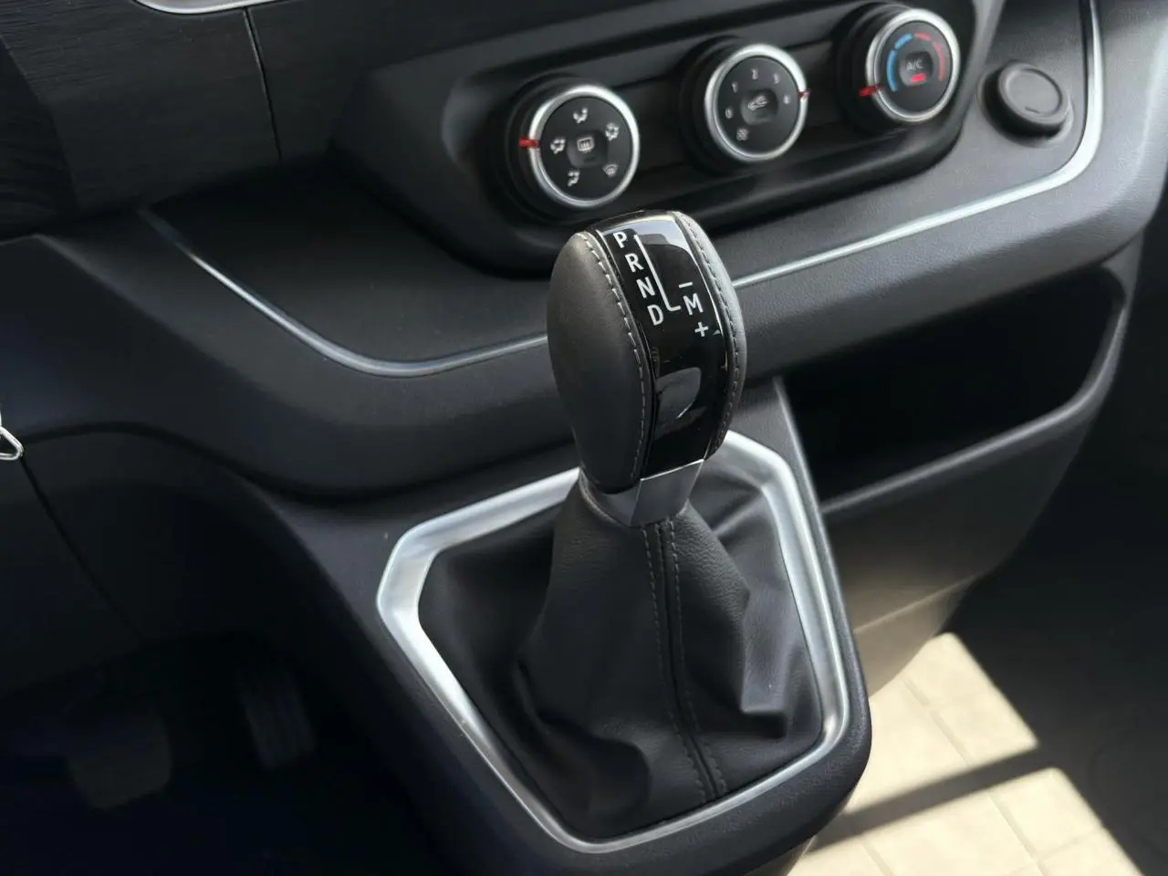 Gros plan sur le levier de vitesses automatique noir et argenté du Renault Trafic Fourgon 2024, avec commandes de climatisation visibles.
