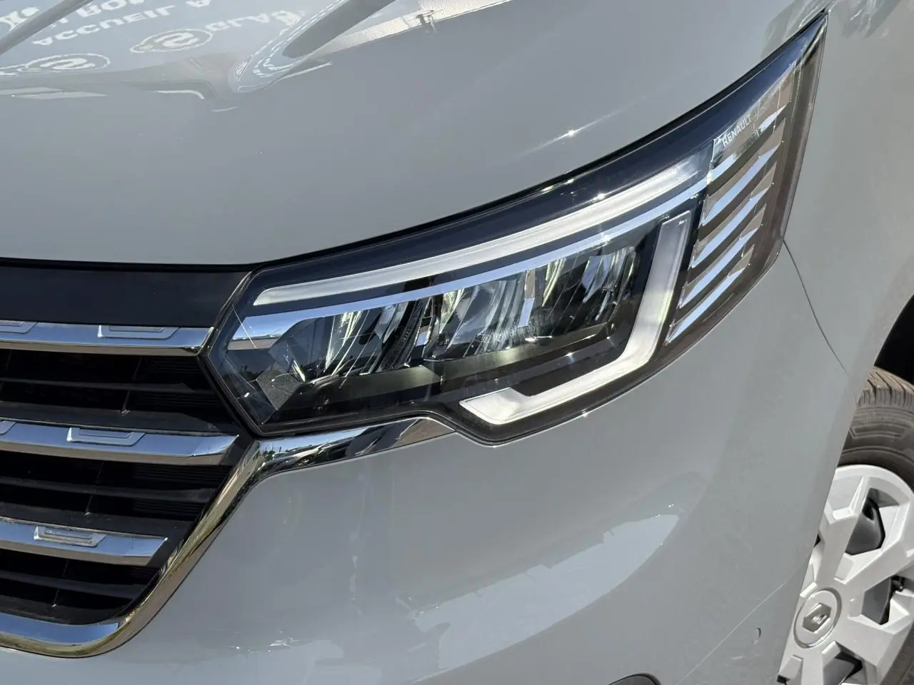 Gros plan sur le phare avant droit et la calandre chromée d'un Renault Trafic Fourgon Urban Grey 2024.