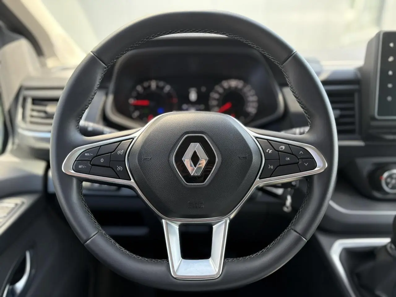 Volant en cuir noir avec logo Renault au centre, tableau de bord flou en arrière-plan, intérieur du Trafic Fourgon 2024.