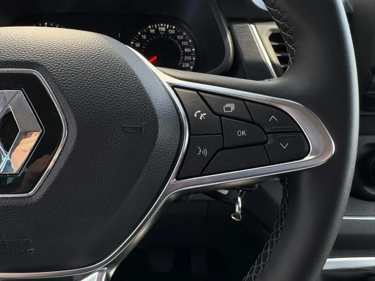 Gros plan sur le volant noir du Renault Trafic Fourgon 2024 avec commandes multifonctions et logo chromé au centre.