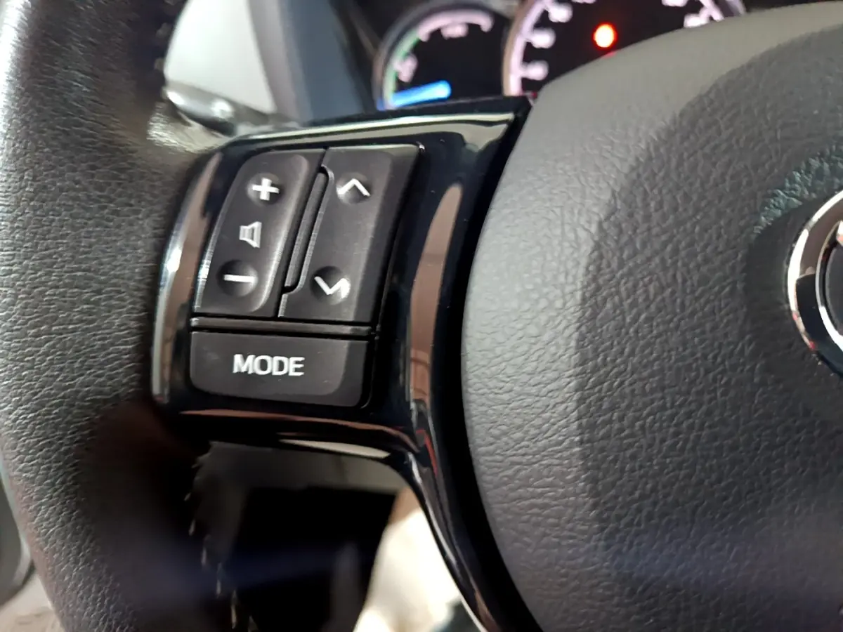 Gros plan sur les commandes gauche du volant cuir noir de la Toyota Yaris hybride blanche, avec tableau de bord en arrière-plan.