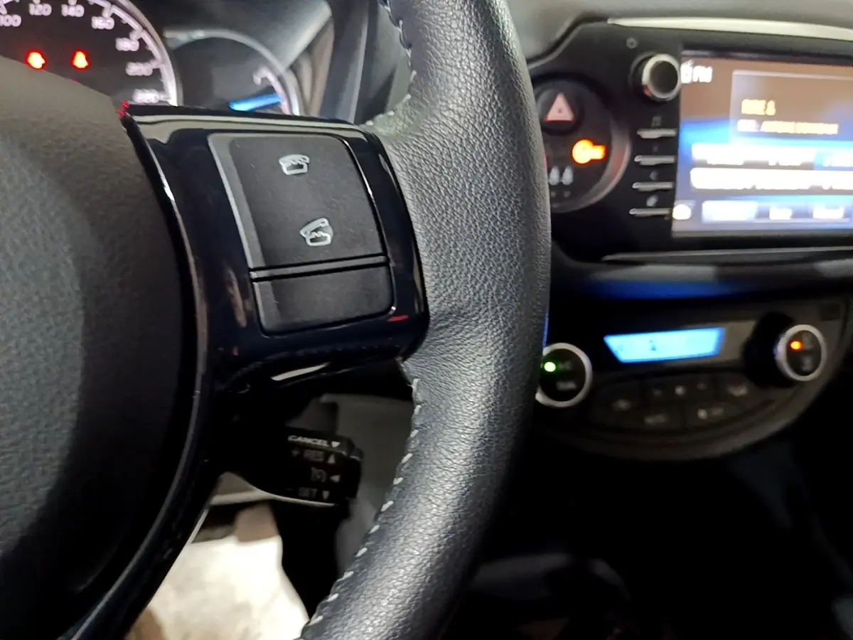 Gros plan sur le volant cuir noir de la Toyota Yaris 2019 avec commandes intégrées et tableau de bord éclairé.