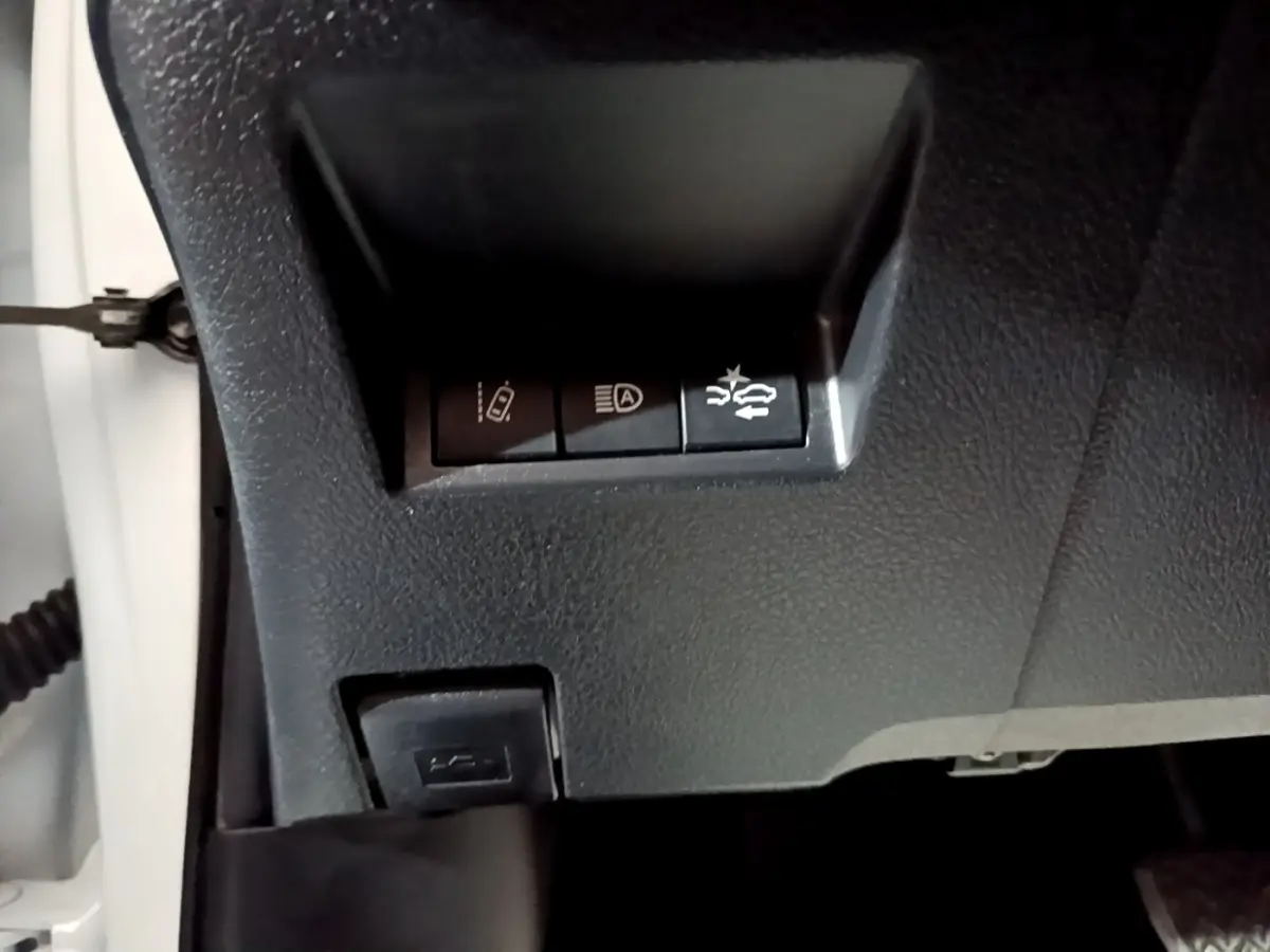 Gros plan sur les commandes de sécurité sous le tableau de bord d'une Toyota Yaris blanche hybride 2019.