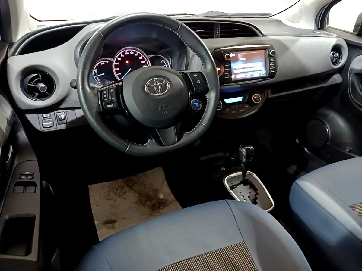 Vue intérieure avant de la Toyota Yaris hybride 2019, volant cuir, écran tactile et sièges tissu bleu visibles.