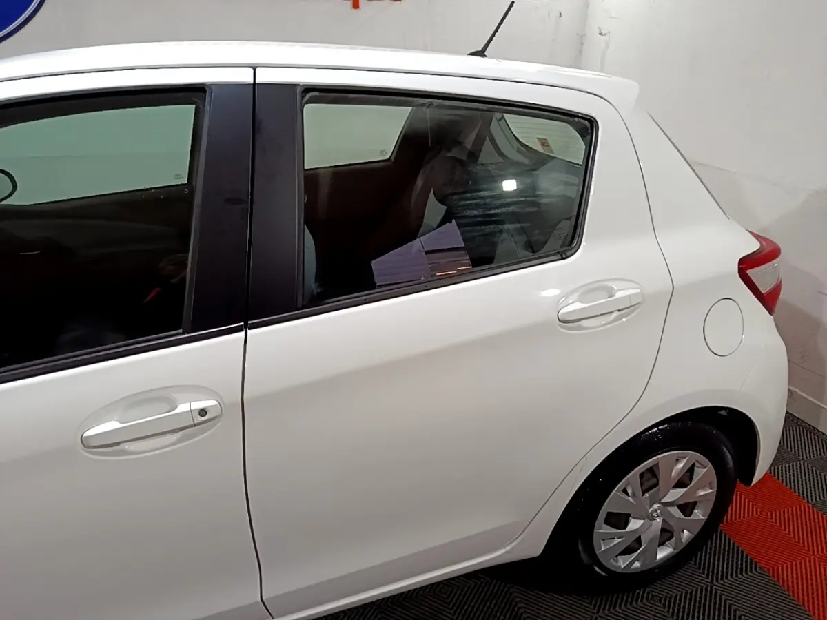 Vue latérale côté droit d'une Toyota Yaris blanche 2019, mettant en valeur la porte arrière et la roue arrière.