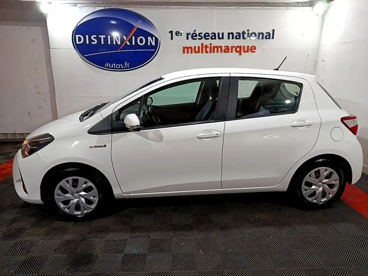 Profil côté gauche d'une Toyota Yaris blanche hybride 2019, avec logo Hybrid visible sur l'aile avant.
