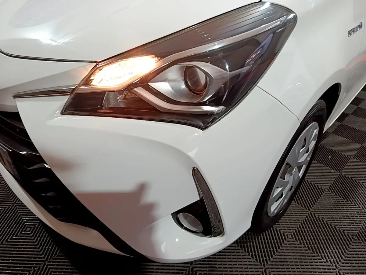 Gros plan sur l'avant droit blanc d'une Toyota Yaris hybride 2019, mettant en valeur le phare allumé et le feu antibrouillard.