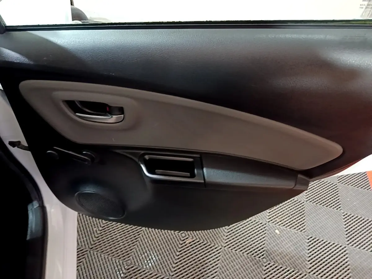 Vue rapprochée de la porte avant gauche blanche de la Toyota Yaris 1.5 Hybrid, avec poignée intérieure et haut-parleur intégrés.