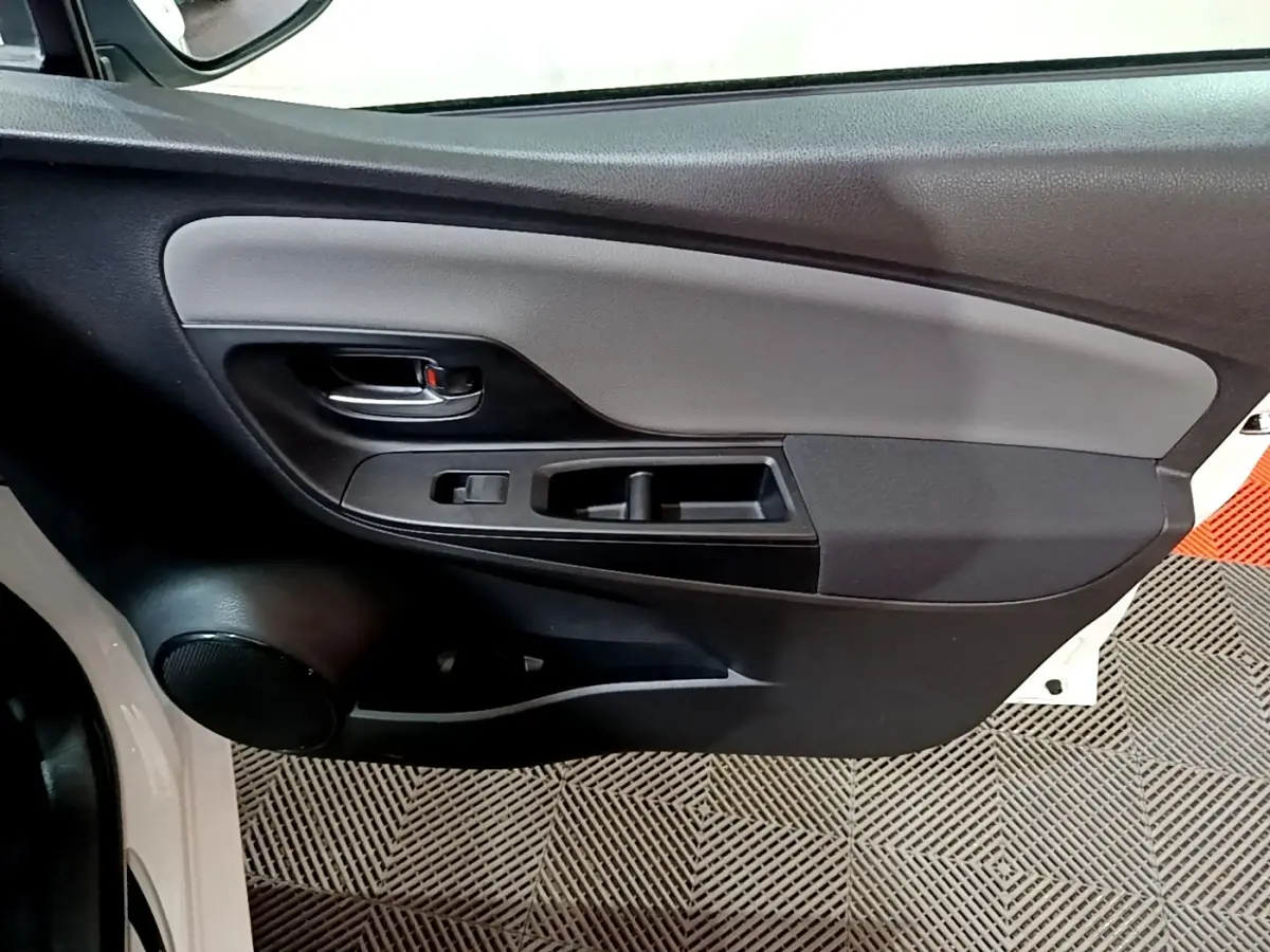 Gros plan sur la porte intérieure côté gauche d'une Toyota Yaris blanche, montrant la poignée et les commandes de fenêtre.