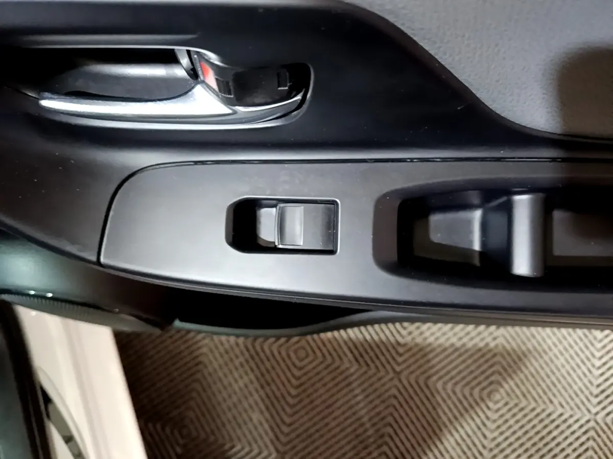 Gros plan sur la poignée intérieure et les commandes de lève-vitre côté conducteur d'une Toyota Yaris blanche 2019.