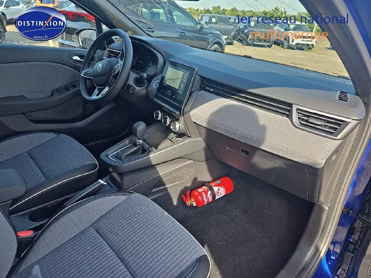 Vue intérieure côté passager de la Renault Clio V bleu iron, avec tableau de bord moderne et extincteur au sol.