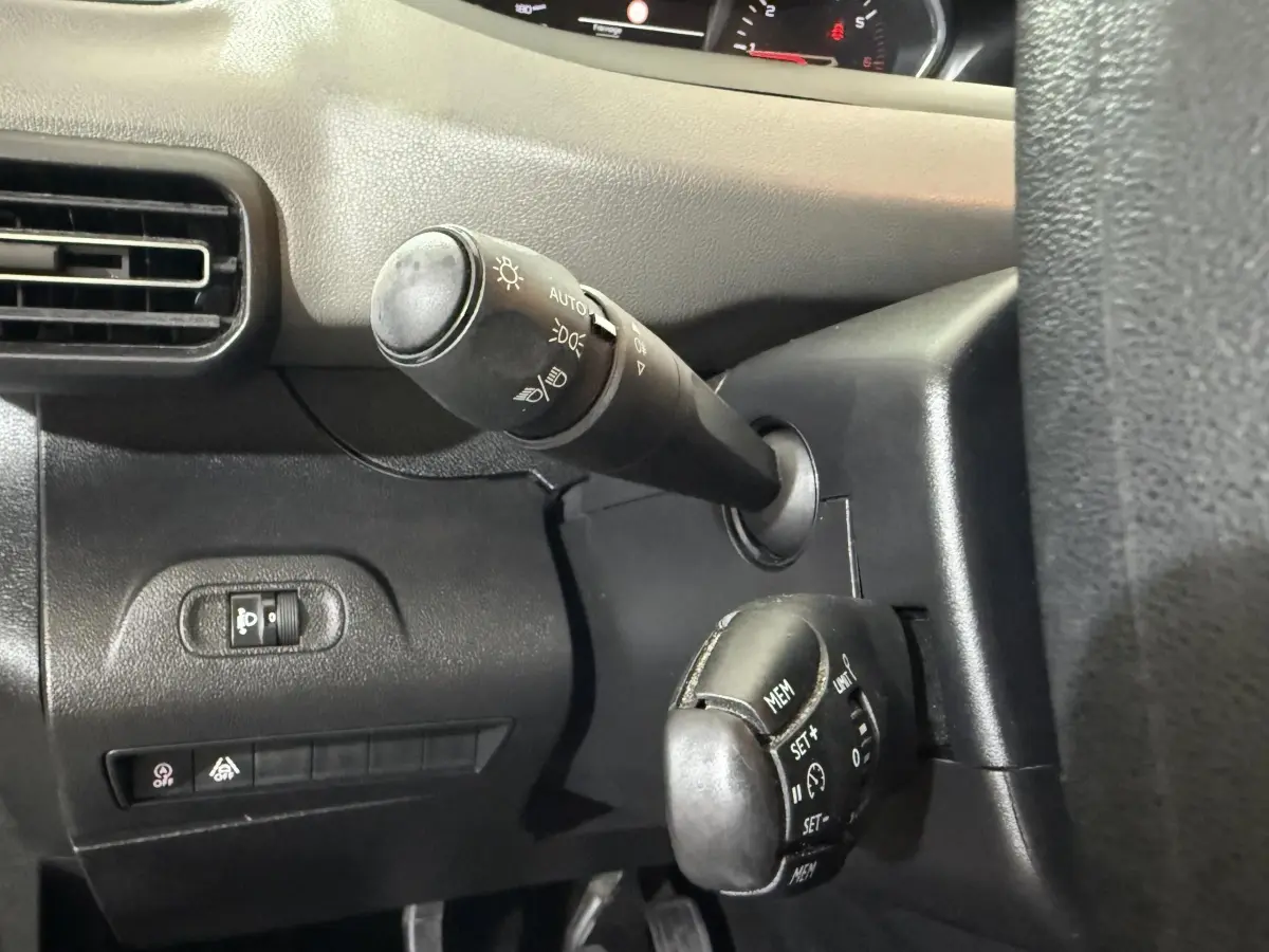 Gros plan sur la commande des phares et régulateur de vitesse à gauche du volant dans l’habitacle noir du Peugeot Rifter blanc 2019.