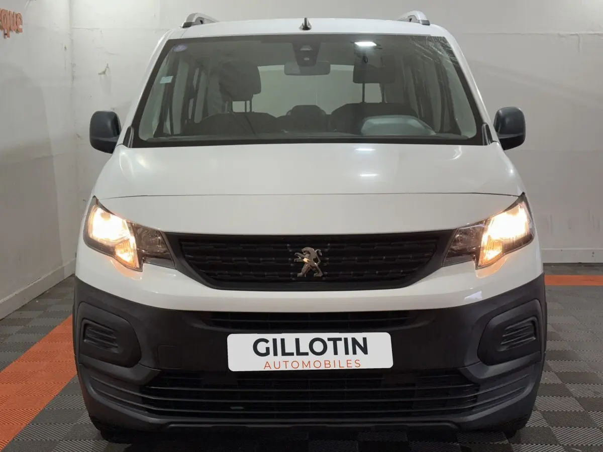 Vue frontale d'un Peugeot Rifter blanc de 2019 avec phares allumés et calandre noire distinctive.