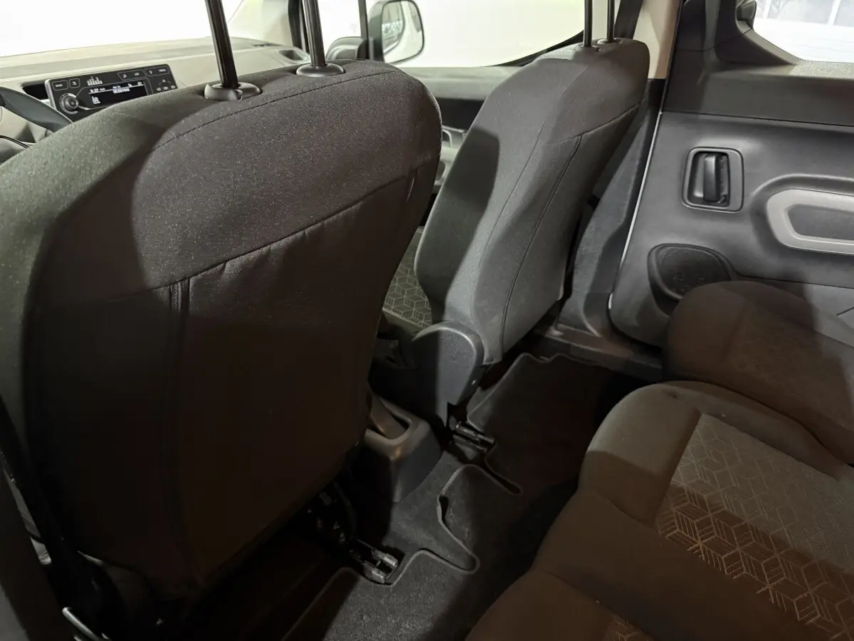 Vue intérieure arrière droite du Peugeot Rifter 2019 blanc, montrant les sièges en tissu noir et la porte latérale.