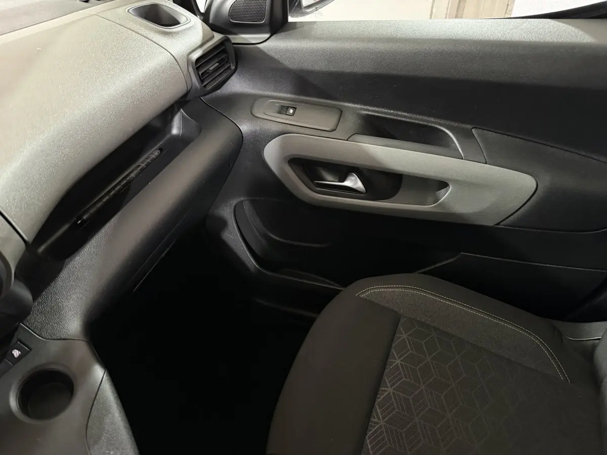 Vue intérieure côté passager du Peugeot Rifter blanc 2019, montrant la porte et le siège tissu noir avec motifs géométriques.