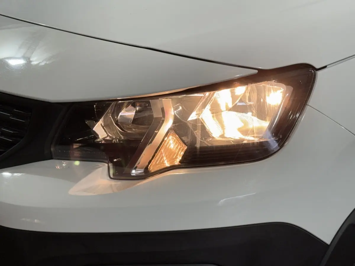 Gros plan sur le phare avant droit allumé d’un Peugeot Rifter blanc, mettant en valeur les détails du bloc optique.