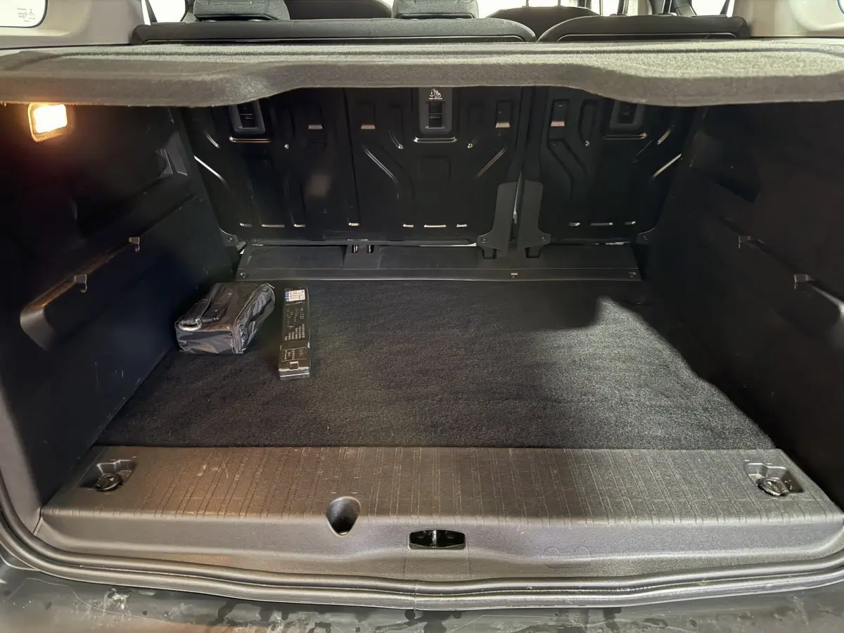 Coffre ouvert vu de l'arrière d'un Peugeot Rifter blanc, montrant un espace de chargement propre avec accessoires rangés.